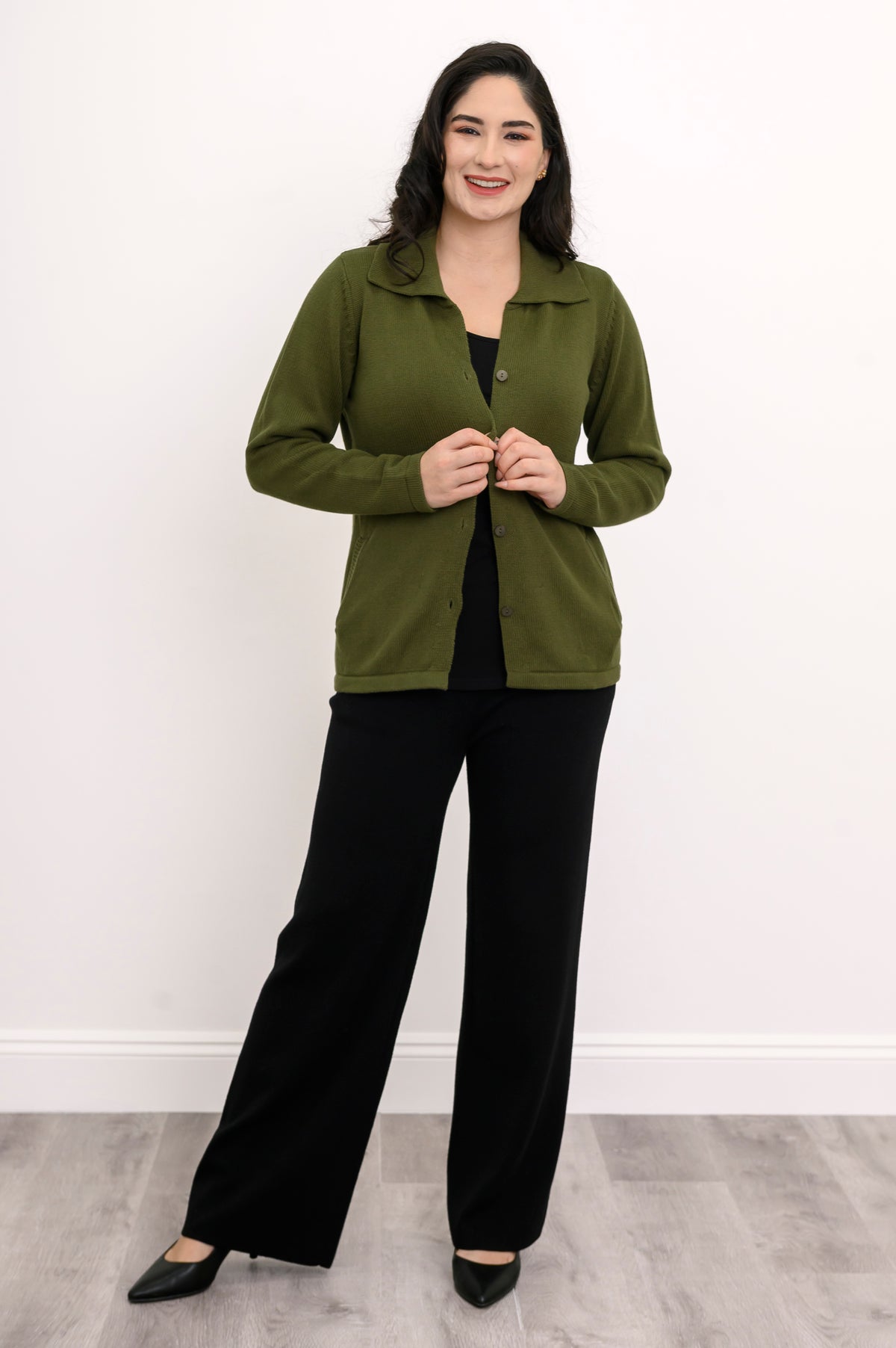 Full length shot of a woman in a fitted 100% cotton cardigan sweater and tailored black pants against a white background.