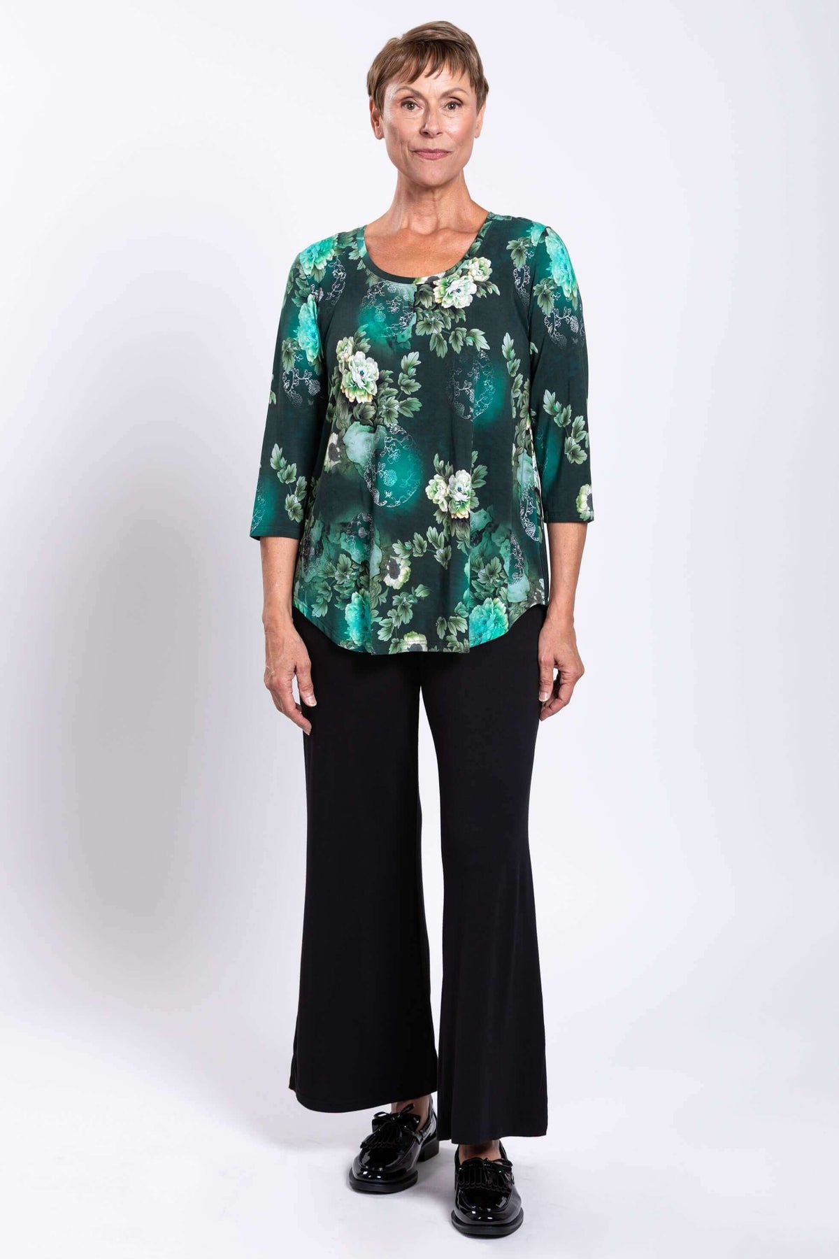 Woman facing forward in green floral bamboo top and black pants, neutral expression