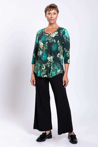 Woman in green floral bamboo top and black pants, angled view, hands by sides