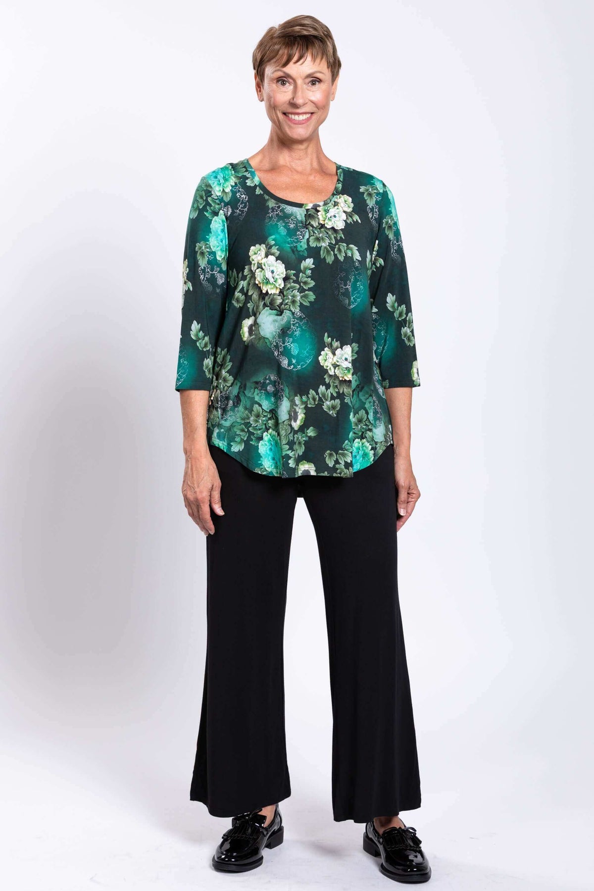 Woman modeling a green floral bamboo top with black pants, full front view, smiling