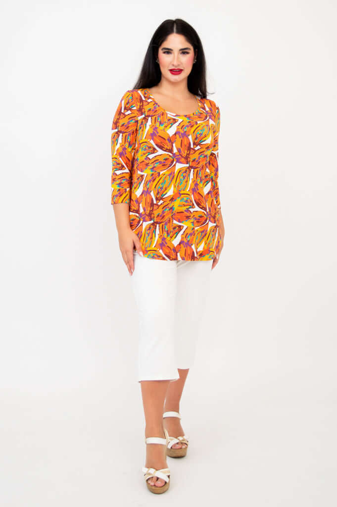 Full front view of a woman in a bright orange bamboo top and white capri pants