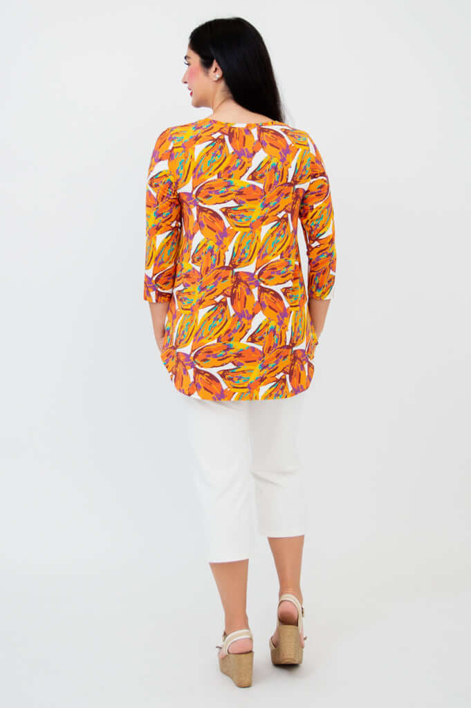 Back view of a woman wearing a vibrant orange leaf print bamboo top with white capris