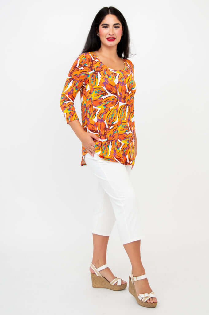 Side view of a woman in an orange patterned top with 3/4 sleeves and white capris