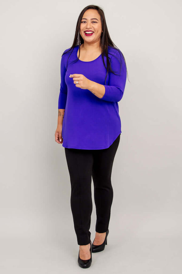 Woman in a purple 3/4 sleeve bamboo top and black pants, walking and smiling.