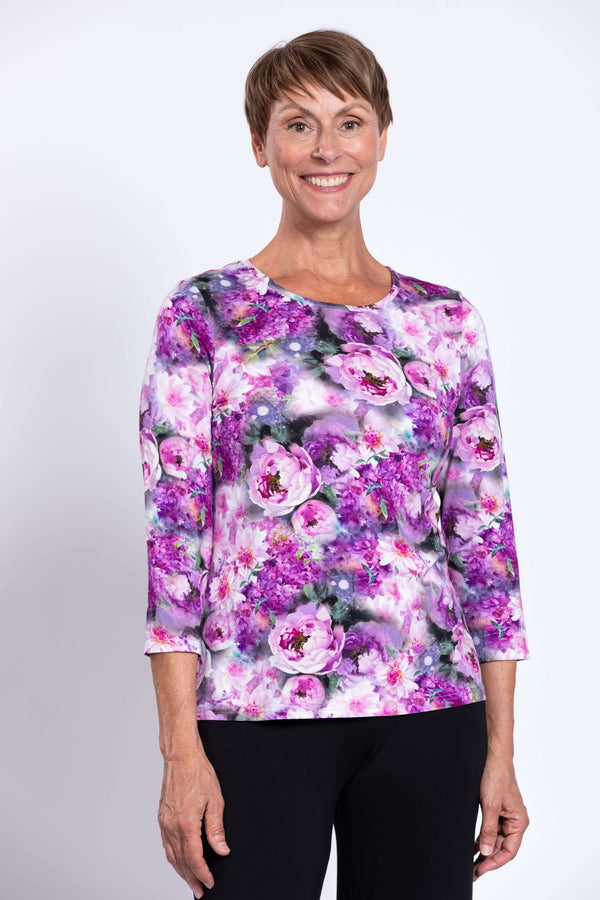 Woman smiling in vibrant floral 3/4 sleeve top with purple and pink flowers