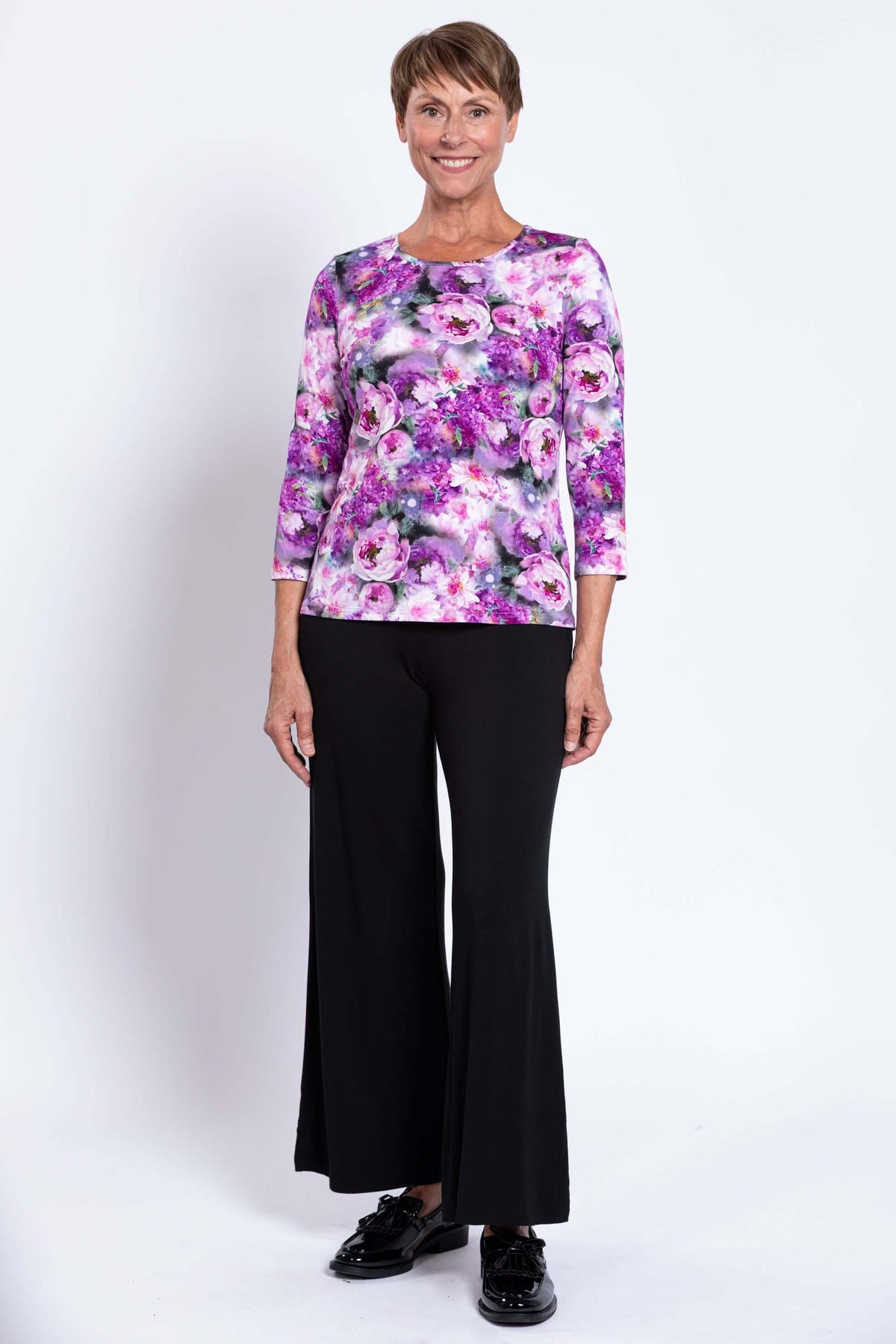 Woman standing in floral 3/4 sleeve top and black pants, smiling