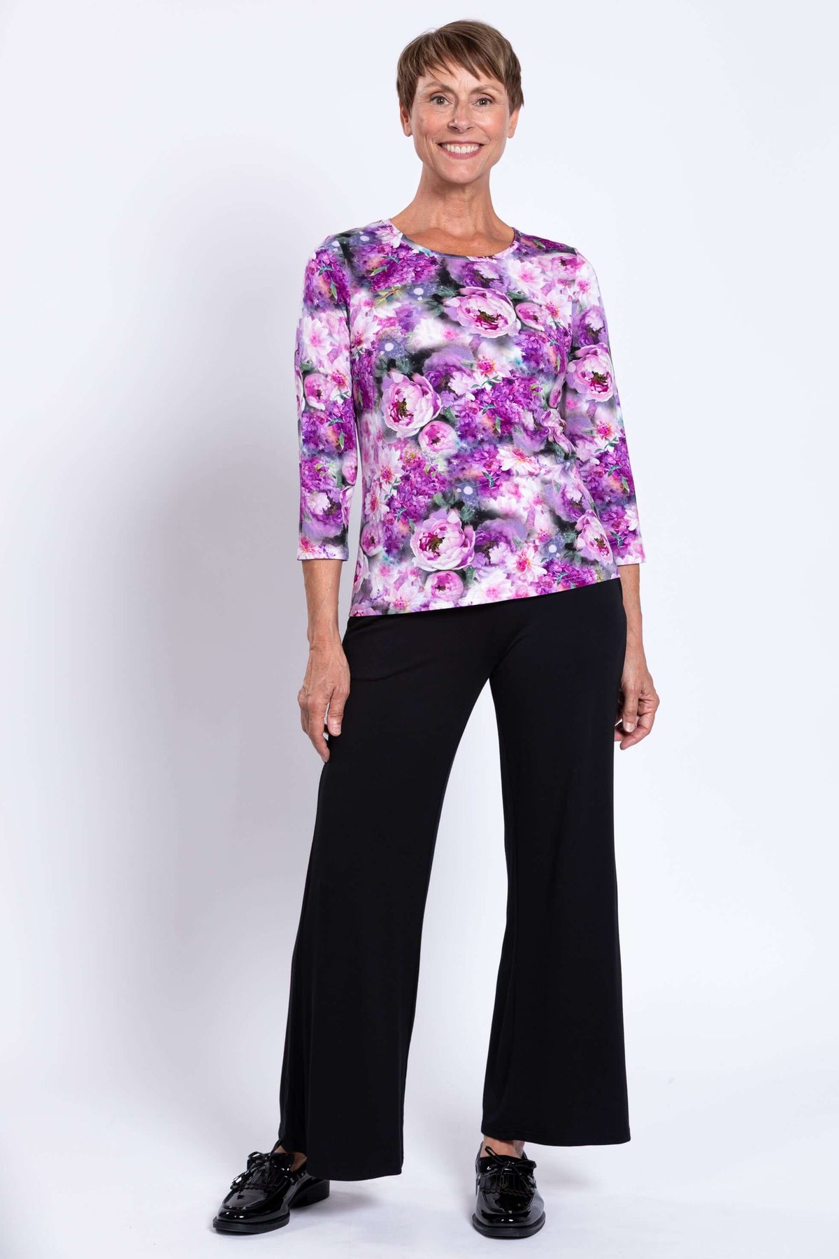 Woman in floral 3/4 sleeve top and black flare pants, smiling