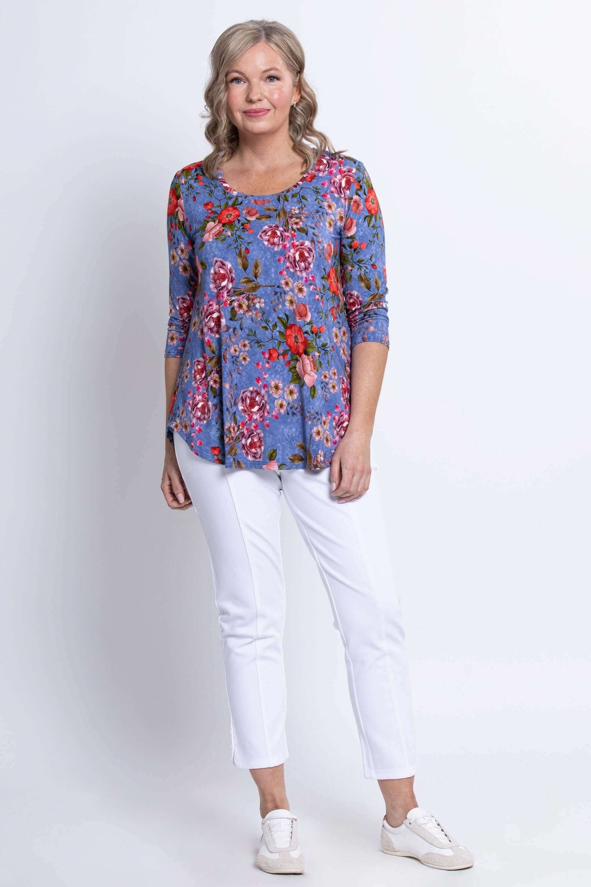 Full body view of a woman in a blue floral 3/4 sleeve top and white pants