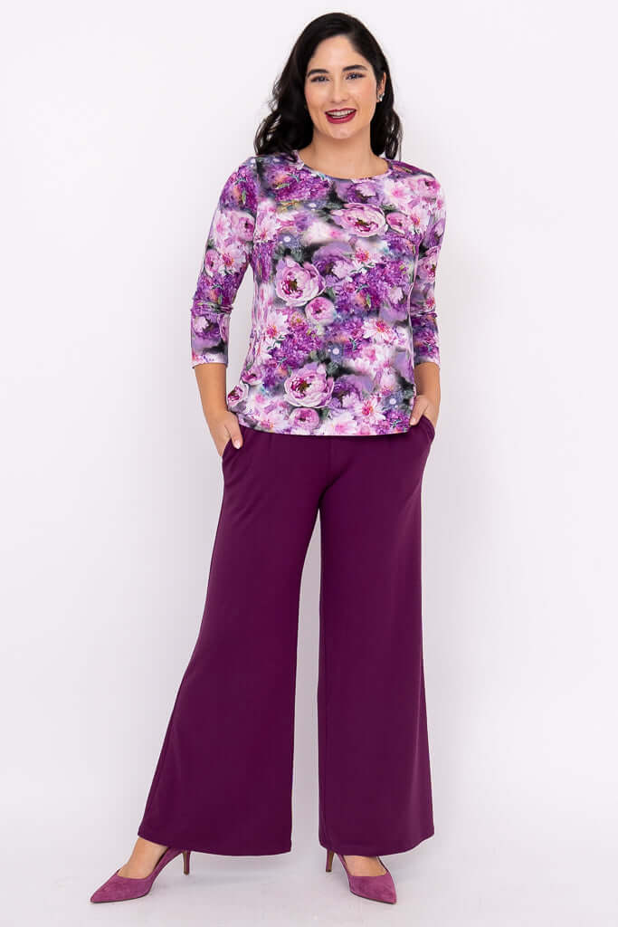 Woman wearing floral 3/4 sleeve top and purple wide-leg pants, hands in pockets