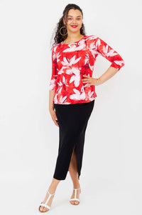 Model in floral 3/4 sleeve top with hand on hip, paired with black skirt and white sandals