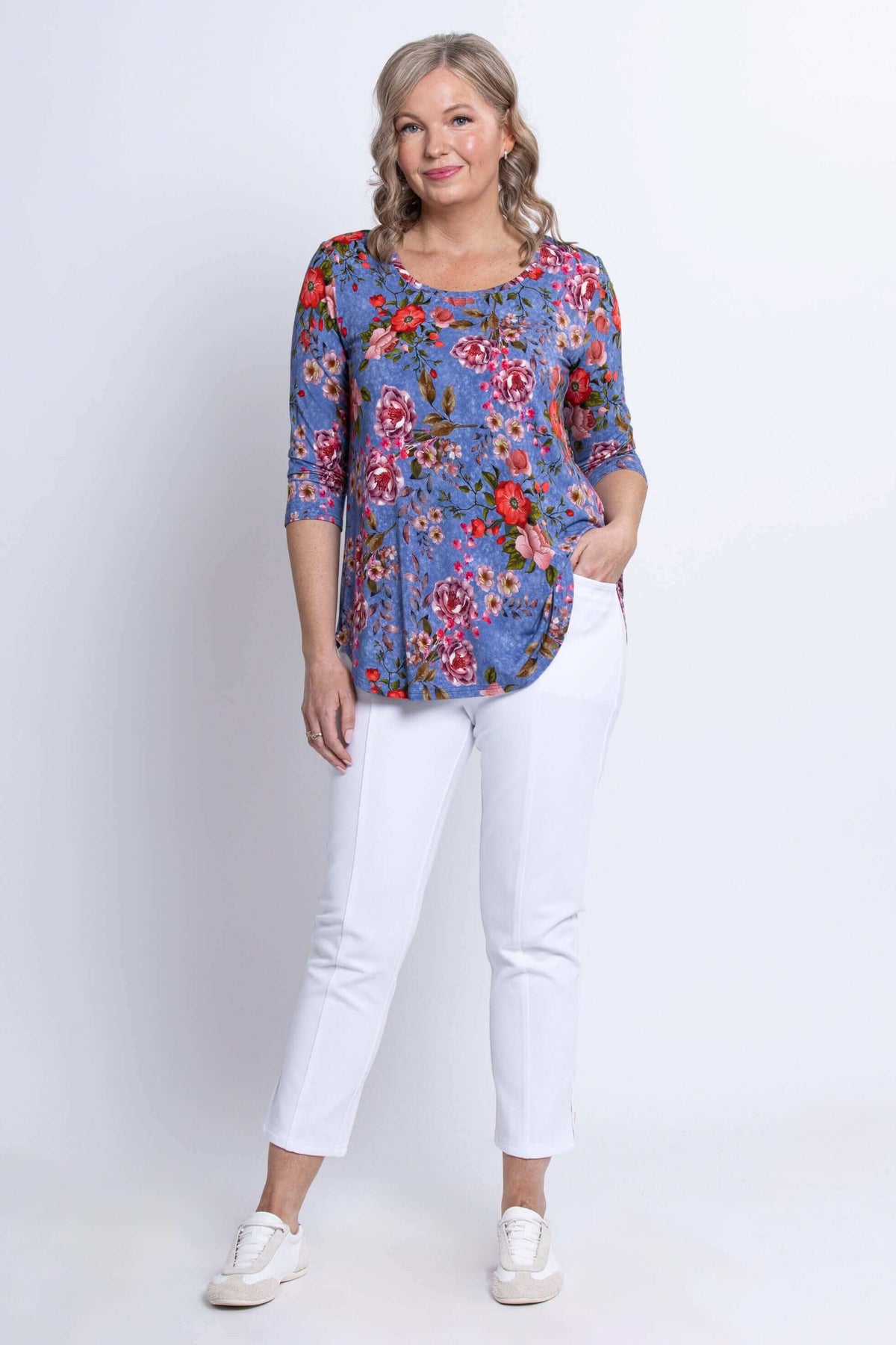 Woman posing with hand in pocket wearing a blue floral 3/4 sleeve top