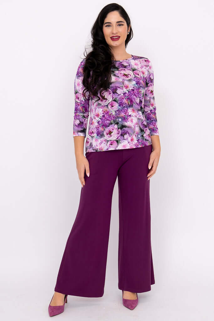 Woman in floral 3/4 sleeve top and purple wide-leg pants, standing with relaxed pose