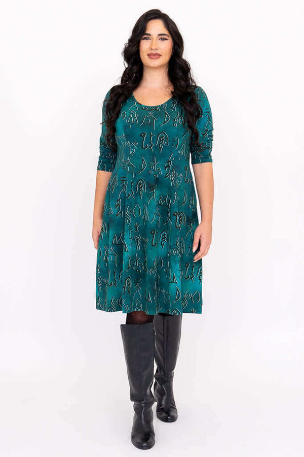 Front view of model wearing teal A-line dress with petroglyph pattern and black boots