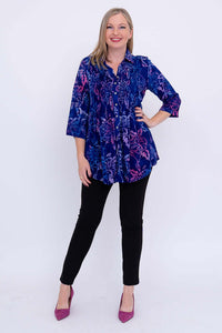 Woman posing front on in blue and purple floral tunic top and black pants
