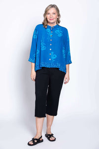 Standing view of a woman in a blue floral blouse with 3/4 sleeves and patterned hem