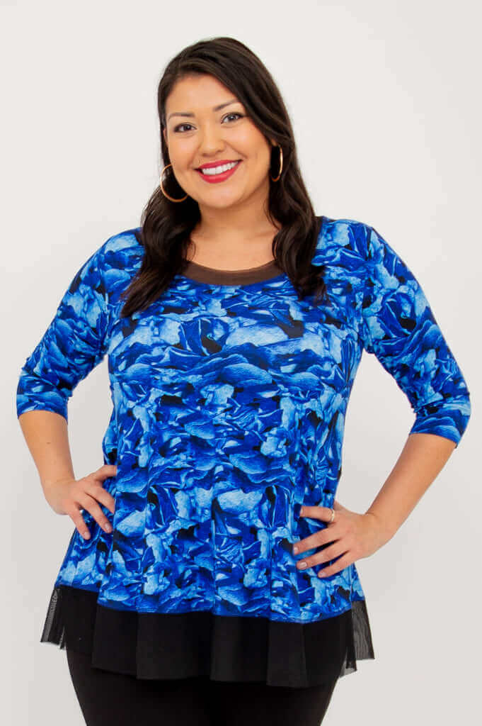 Woman wearing a blue floral top with mesh accents and 3/4 sleeves, smiling