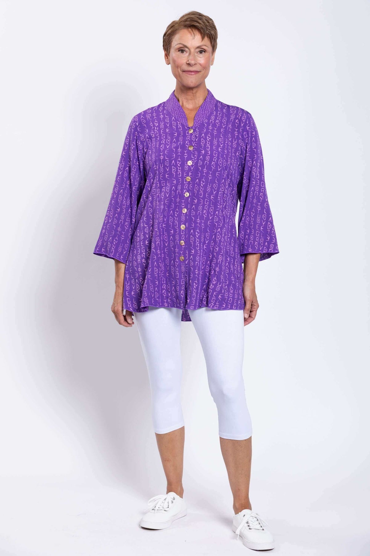 Full front view of woman in purple patterned blouse with 3/4 bell sleeves and white leggings
