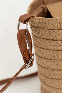Detail of adjustable brown leather strap on woven straw tote bag