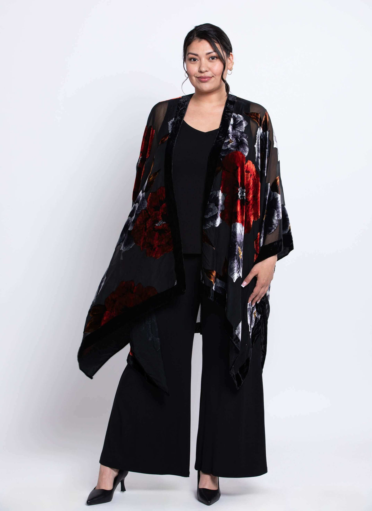 Woman wearing a draped black floral kimono cover-up with red and grey blooms, angled front view