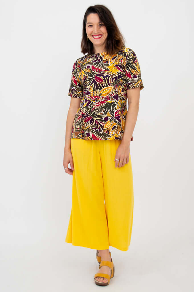 Smiling woman in a multicolor printed tee and yellow wide-leg pants, angled front view