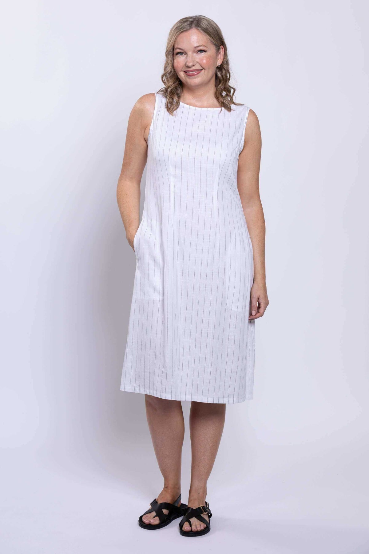 Front angled view of woman posing in a white sleeveless striped dress with pockets