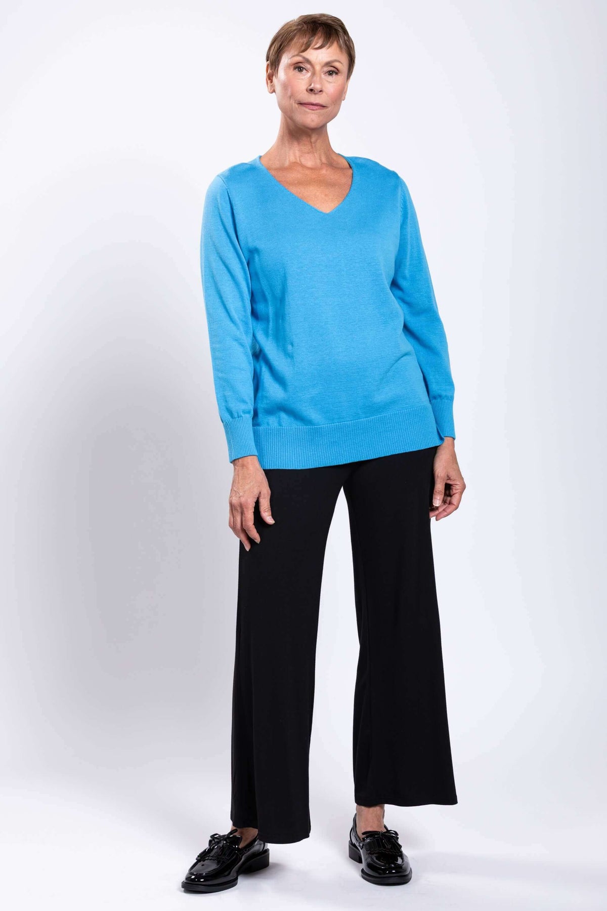 Angled front view of woman in blue cotton V-neck sweater and black wide-leg pants