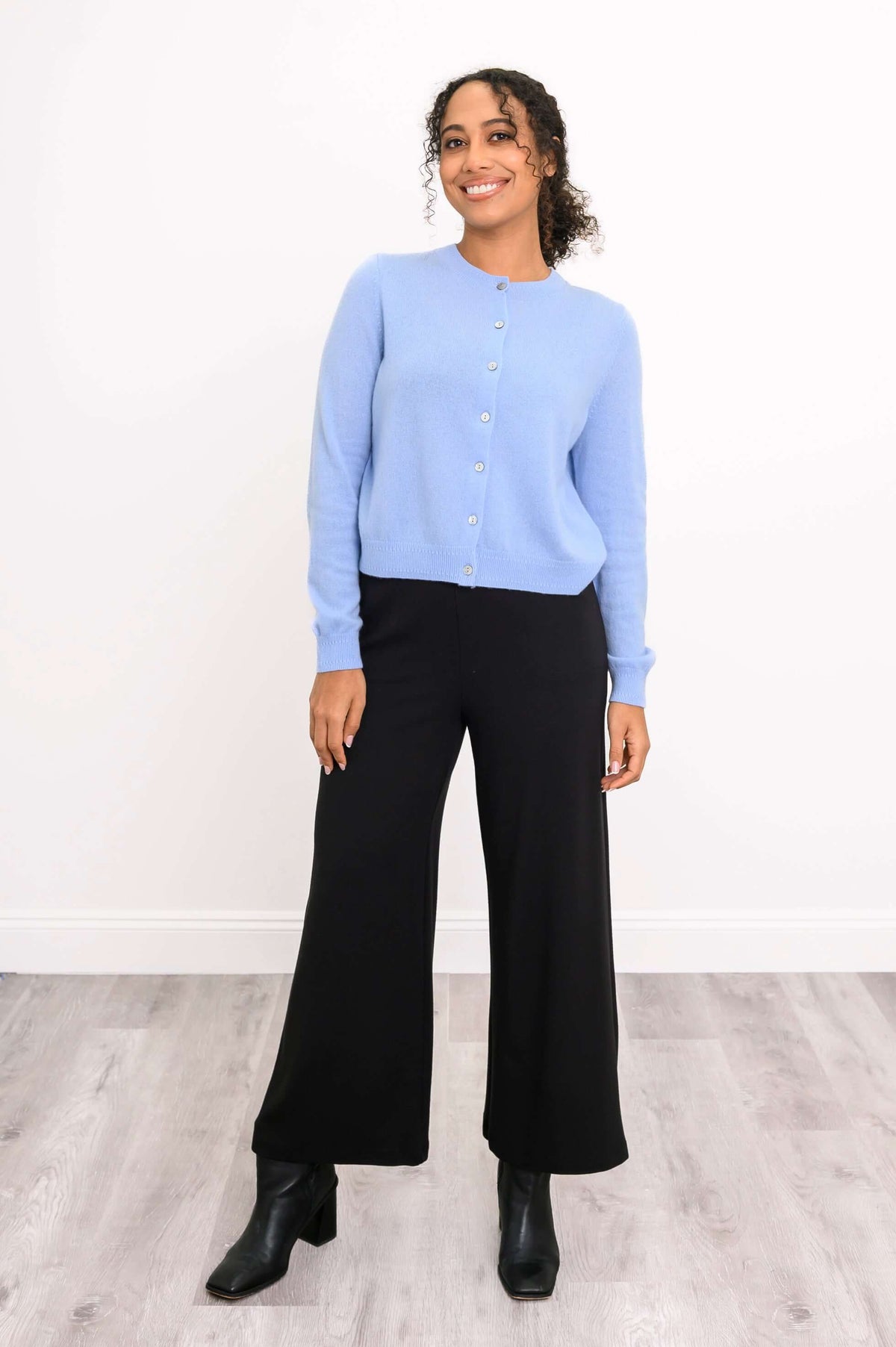 Woman standing in a light blue cashmere cardigan and black pants, angled front view