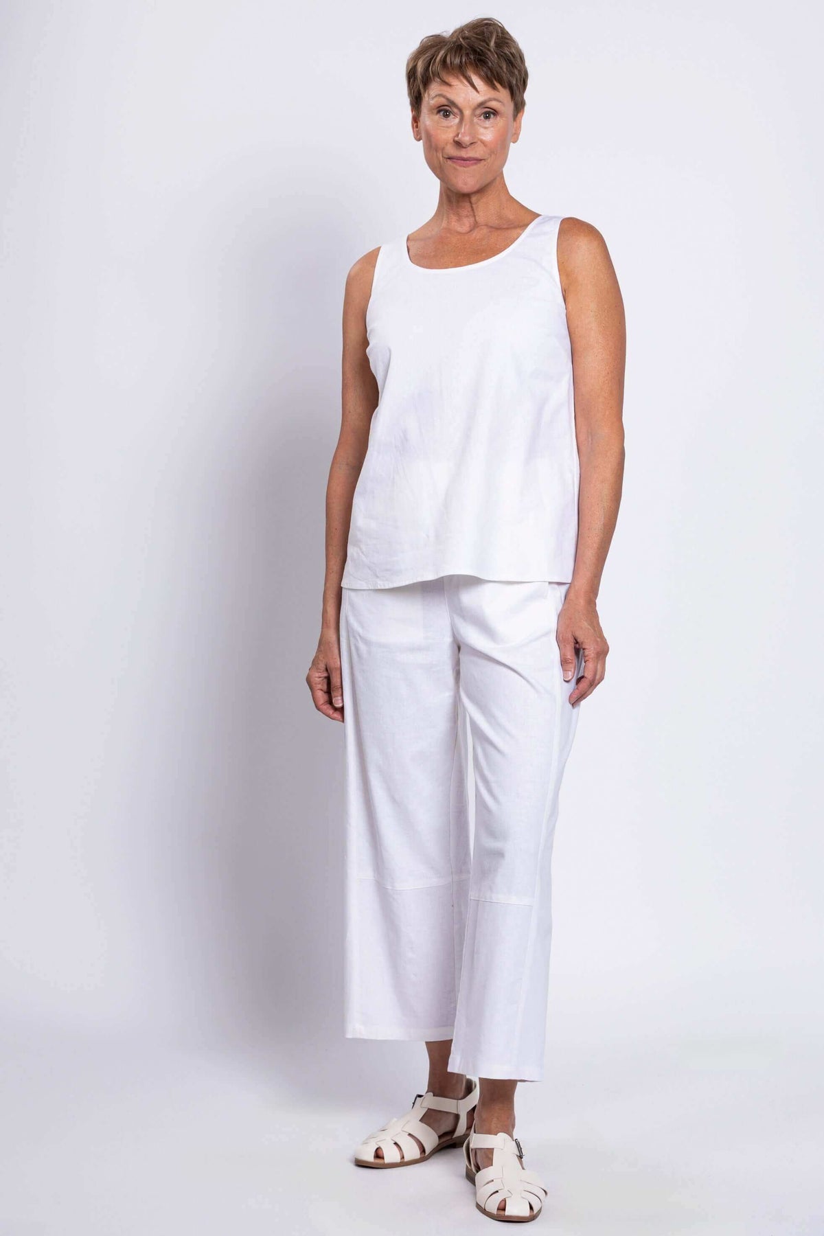 Angled front view of woman in white linen tank top and pants