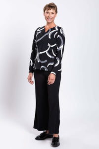 Full body angled view of woman smiling in black and white abstract print top
