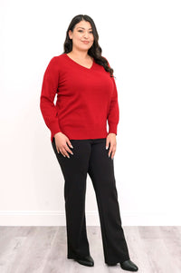 Angled front view of woman in red V-neck sweater and black pants