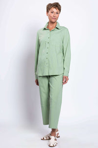 Angled view of a woman wearing a sage green shirt and pants, standing casually