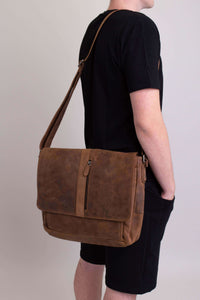 Man with hands in pocket carrying brown buffalo leather messenger bag, angled side view