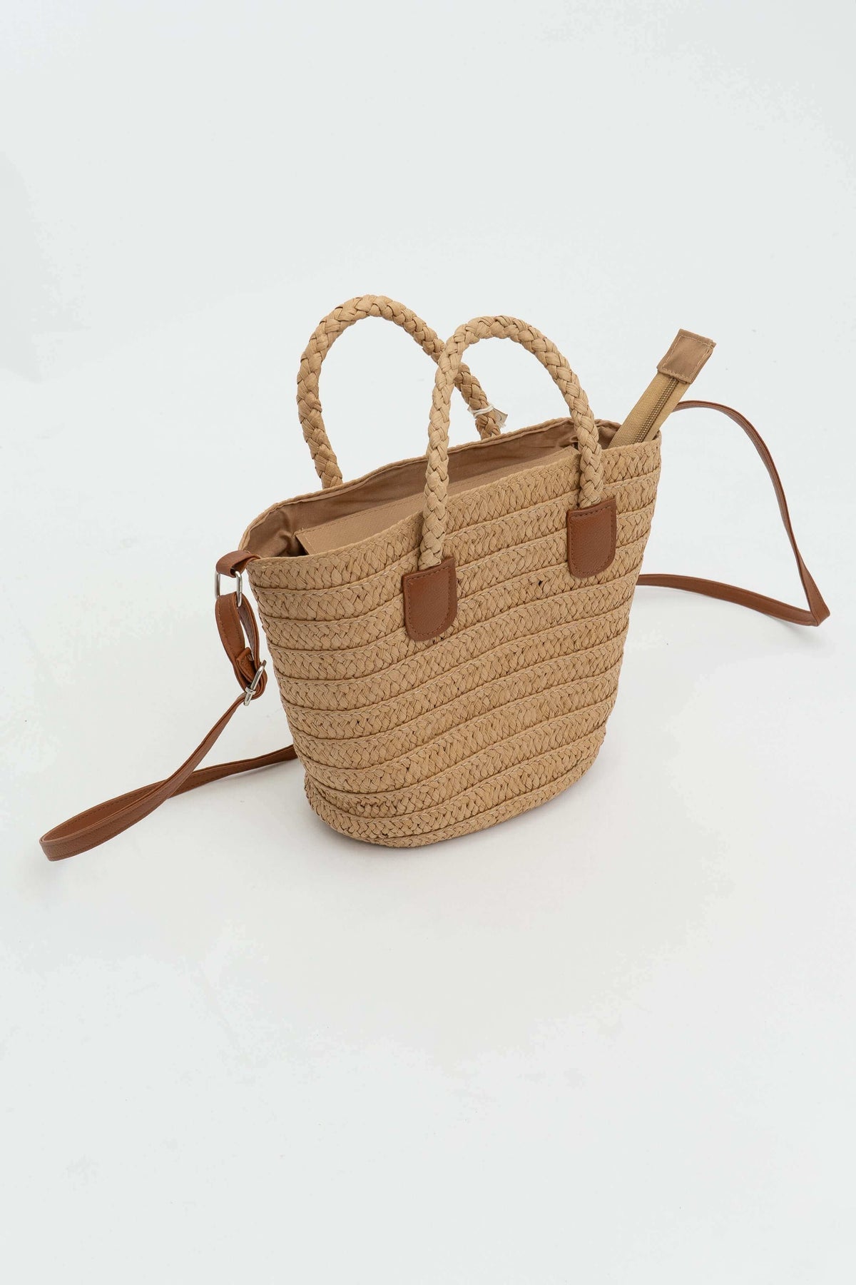 Angled side view of woven straw tote bag with braided handles and leather strap