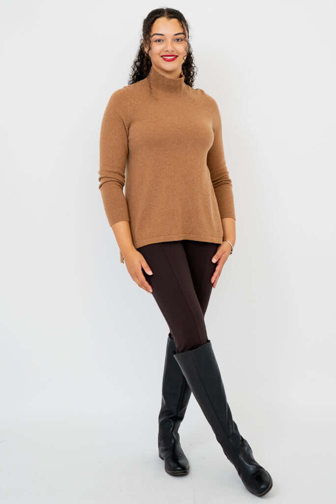 Angled view of woman in camel sweater and black knee-high boots