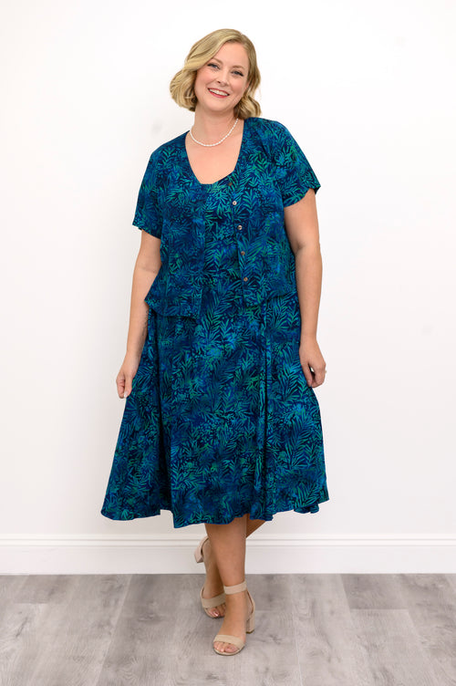 Woman wearing a blue patterned dress and blue patterned blouse against a white background, front view