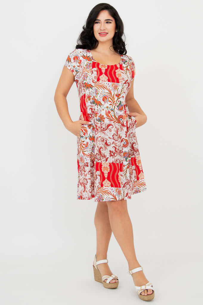 Woman wearing Anna dress with red paisley print, hands in pockets, angled view