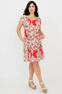 Woman wearing Anna dress with red paisley print, hands in pockets, angled view