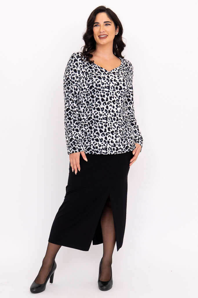 Model in Annette leopard print top and black skirt, standing and smiling