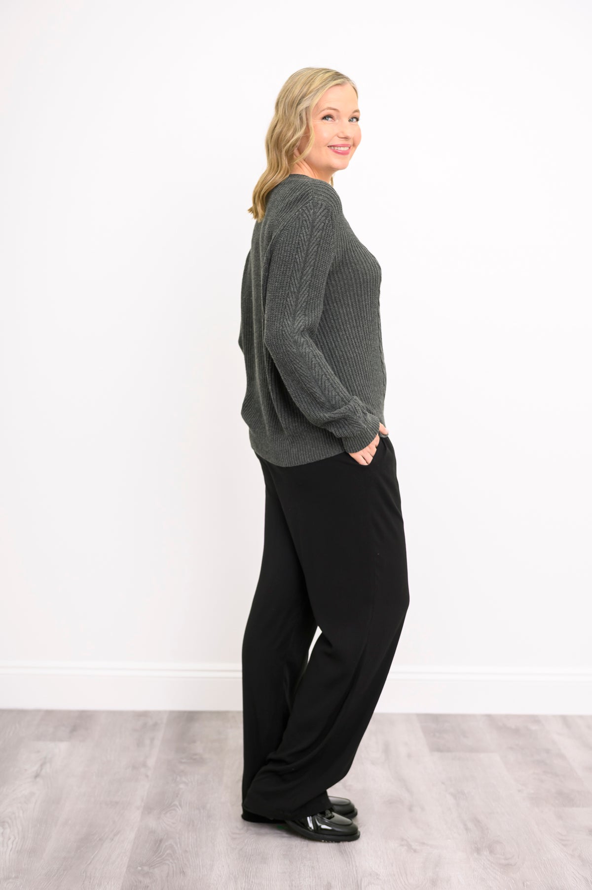 Side-angle view of a slate-colored knit sweater, showcasing comfortable long sleeves and a clean waist hem.