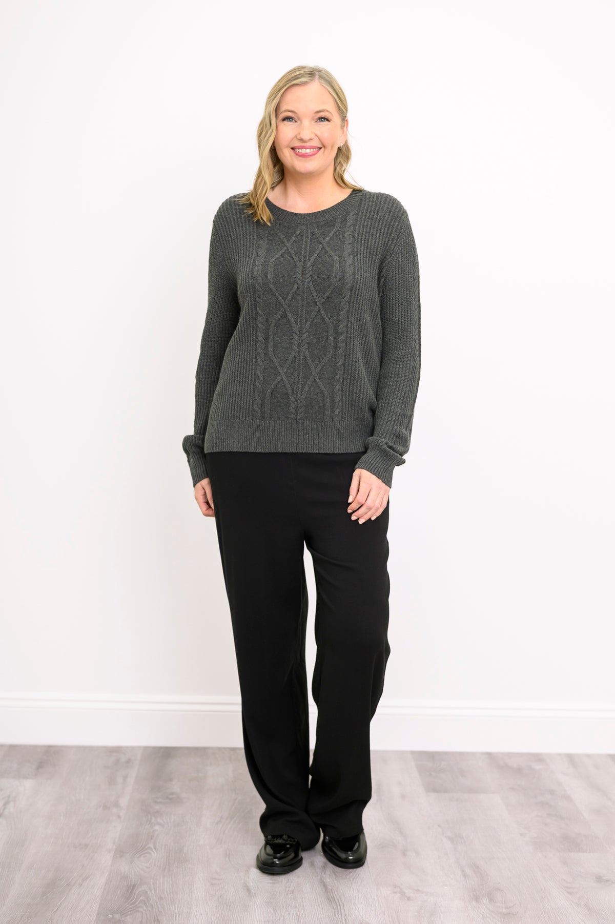 Front view of a women's graphite long-sleeve knit top, showcasing a textured plaited pattern on a model.