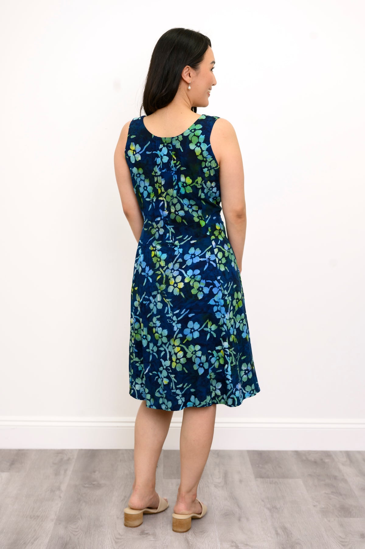 Back view woman wearing blue and green floral patterned sleeveless dress on a white background