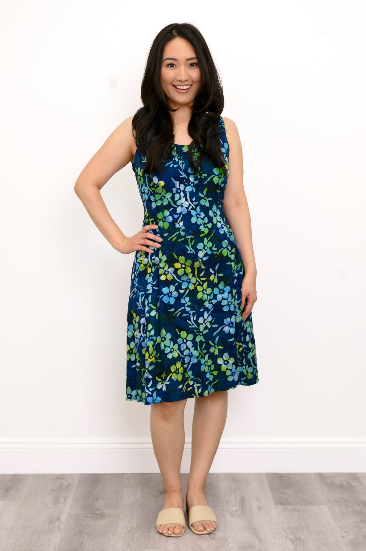 Front view woman wearing blue and green floral patterned sleeveless dress on a white background