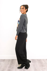 Side view of mode wearing grey/multicolor argyle print sweater and relaxed fit pants