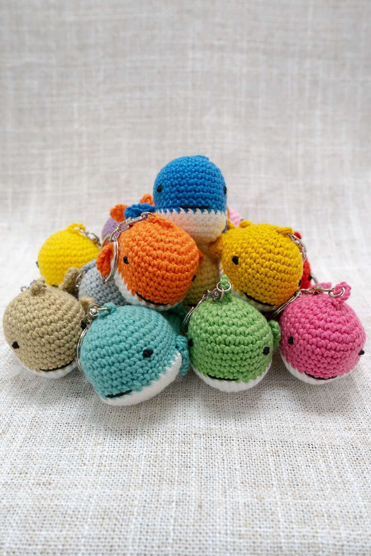 Pile of assorted colourful handmade crochet animal keychains on neutral fabric