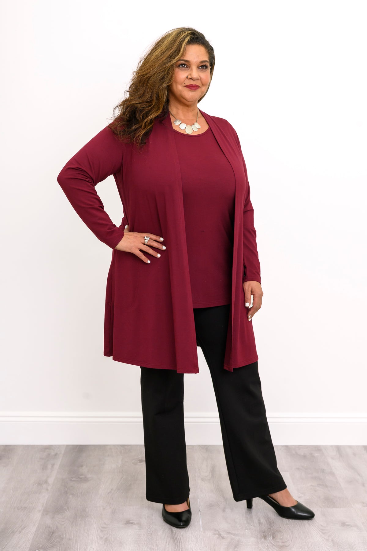 Full-length front view of a woman styling an open wine red bamboo cardigan with a matching burgundy top and black pants.