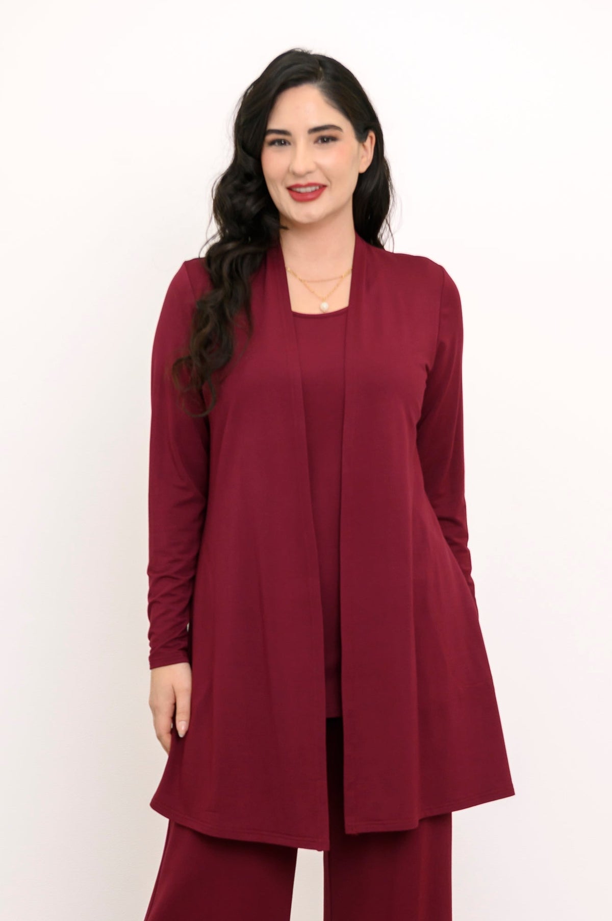 Full-length portrait of a woman wearing an open burgundy bamboo cardigan with matching wine red knit pants.