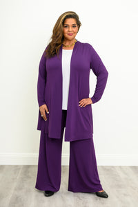 Full-length view of a woman wearing an open royale purple bamboo cardigan layered over a white shirt and purple pants.
