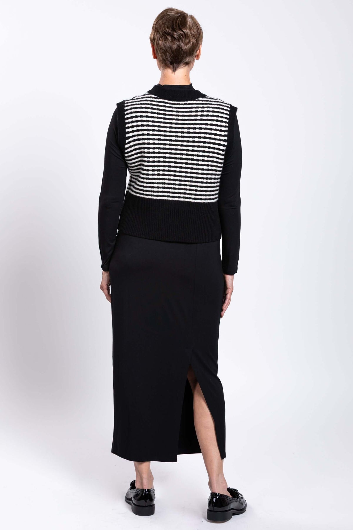 Back view of model wearing black and white striped vest with black skirt