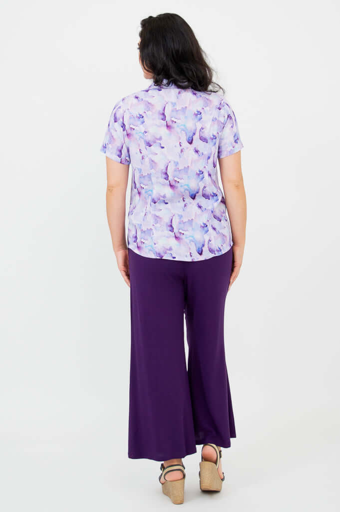 Back view of woman wearing a purple watercolor short sleeve shirt and purple pants