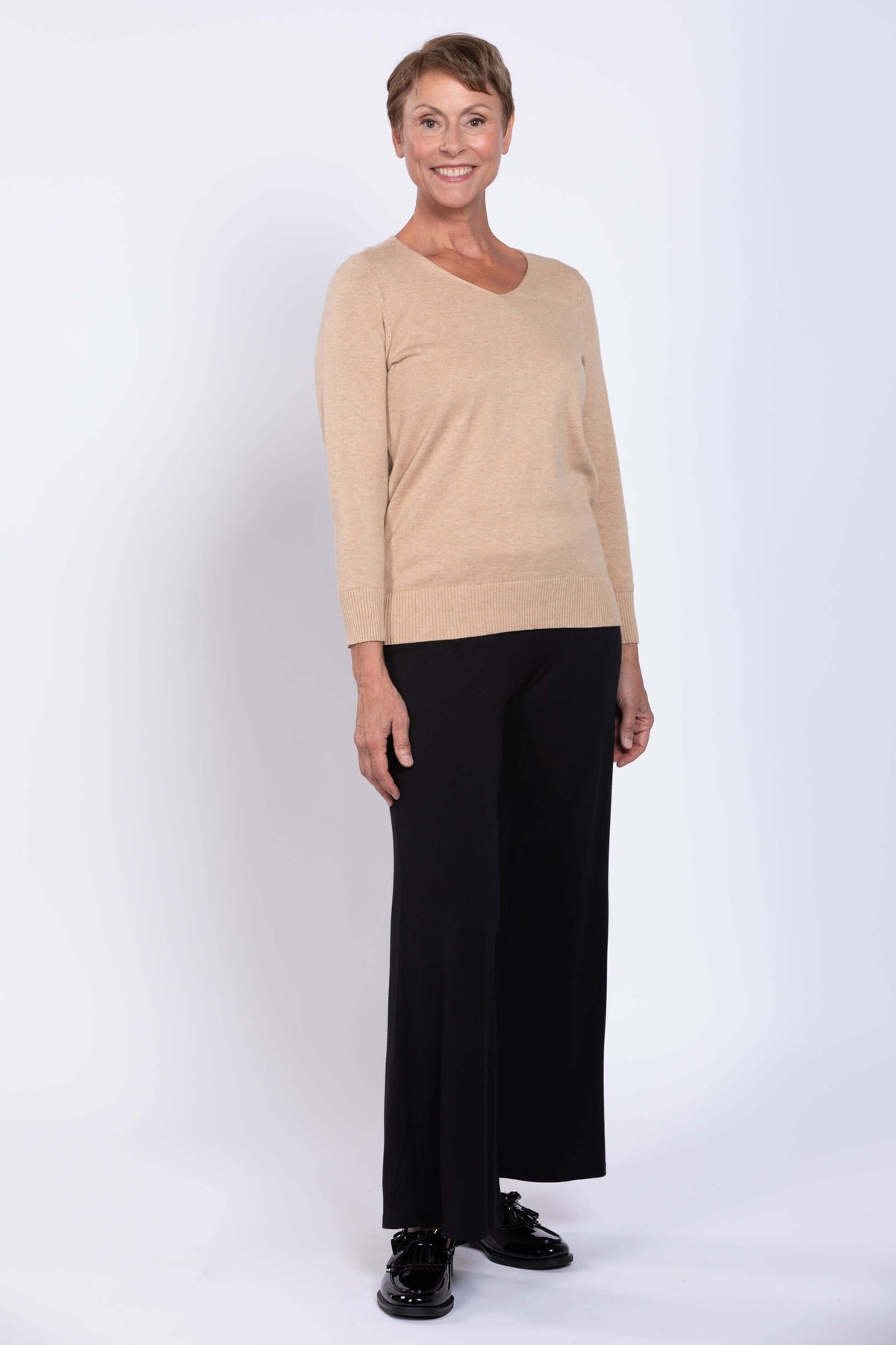 Back view of woman wearing beige V-neck sweater and black pants